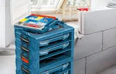 Stacked blue toolboxes with an open organizer tray holding screws and wall plugs nearby.