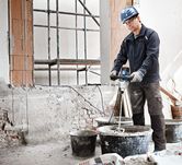 A person wearing safety equipment mixes construction material with a stirring mechanism.