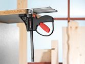 System accessory clamp securing a wooden board to a metal surface in a workshop.