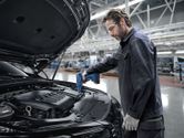 A person wearing safety equipment uses a heat gun on an automotive assembly line.