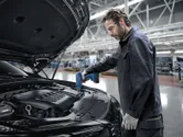 A person wearing safety equipment uses a heat gun on an automotive assembly line.