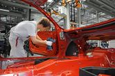 A person wearing safety equipment uses a cordless drill to assemble a car door in a factory.