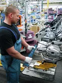 A person wearing safety equipment uses a power tool to assemble a motorcycle engine.