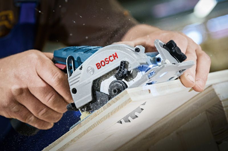 A person trims a wooden board using a cordless circular saw.