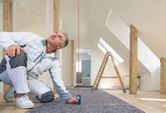 Person in work clothes uses a laser measure to check vertical distance in a renovated room.