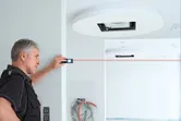 A person uses a laser measure to align distances on an indoor construction site.