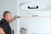 A person measures a room’s length with a laser measure in a bright indoor space.