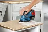 A person operates a cordless orbital sander on a smooth surface.