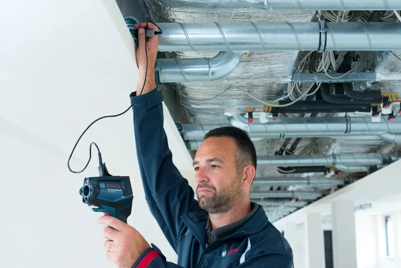 GIS 1000 C A person inspects ventilation pipes in a ceiling using an inspection camera.