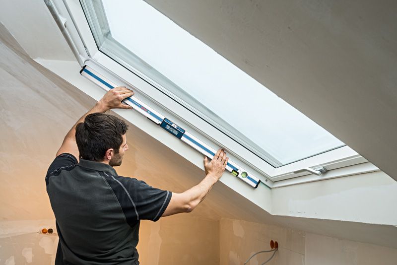 GIM 120 Person measuring window angle with a digital inclinometer in a finished attic room.