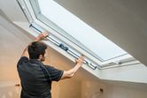 Person measuring window angle with a digital inclinometer in a finished attic room.