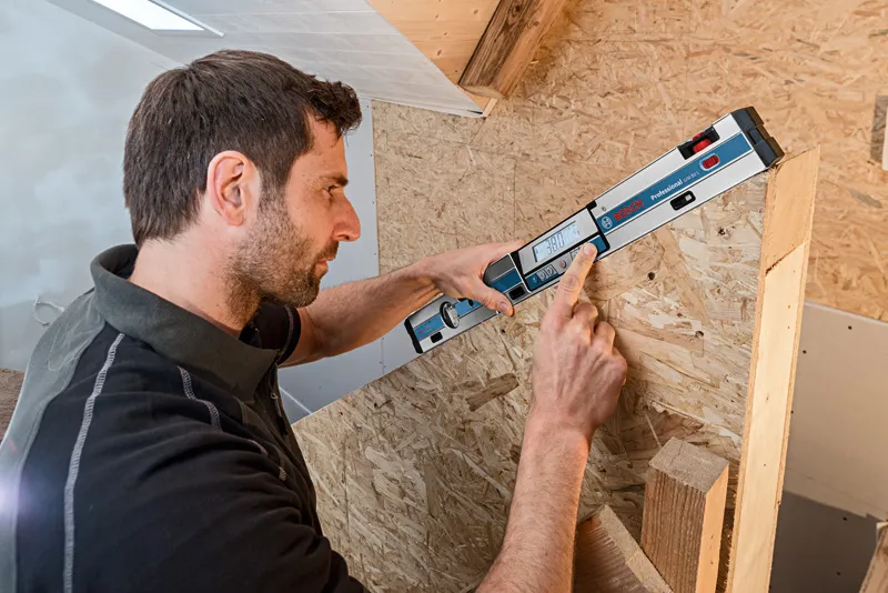 Person measuring an angled wooden surface using a digital inclinometer.