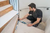 A person measures stair angles using an angle measurer on a staircase.