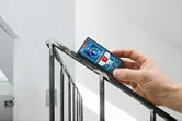 A person measures the angle of a stair railing with a laser measure.