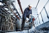 A person wearing safety equipment operates a cordless rotary hammer on a concrete slab.