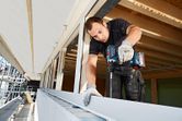 A person wearing safety equipment drills into a metal frame at a building site.