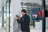 A person aligns a laser receiver on a concrete pillar in a modern office.