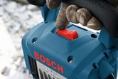 Person wearing safety equipment presses a red switch on a blue power tool.