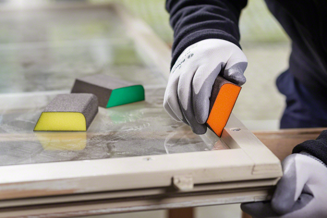 Foam abrasives S471 std block-M Worker wearing safety equipment sanding a window frame with a sanding sponge.