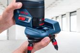 Person adjusts a laser leveling tool accessory in a bright, unfinished room.