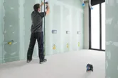 Person adjusting pipe on unfinished wall, green laser leveling tool projecting horizontal line.