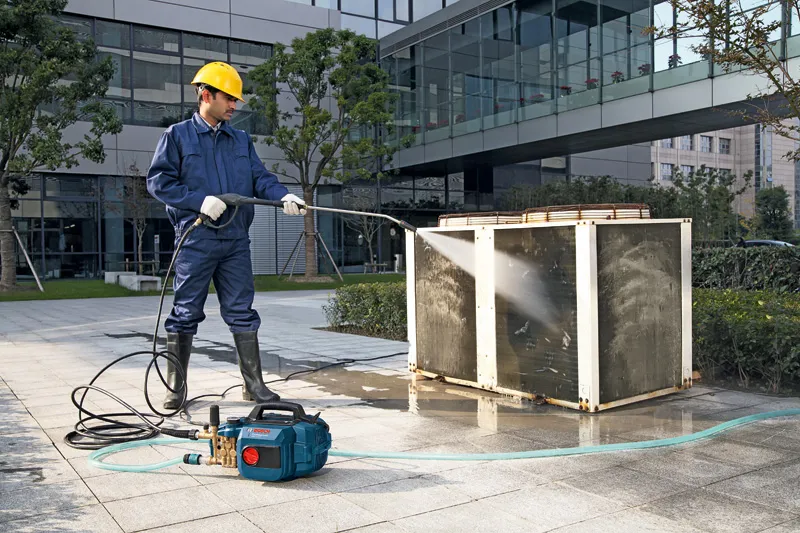 GHP 5-13 C A person wearing safety equipment uses a high-pressure washer to clean an outdoor unit.