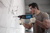 A person wearing safety equipment drills into a concrete wall with a power tool.