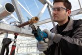 A person wearing safety equipment cuts a metal pipe with a reciprocating saw.
