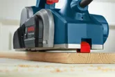 Electric planer smoothing a wooden board on a workshop table.