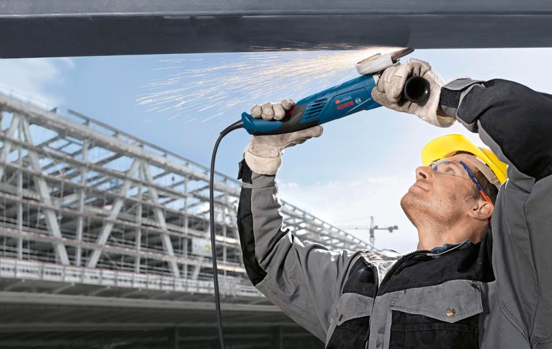 GWS 18-125 L A person wearing safety equipment grinds overhead metal, producing sparks.