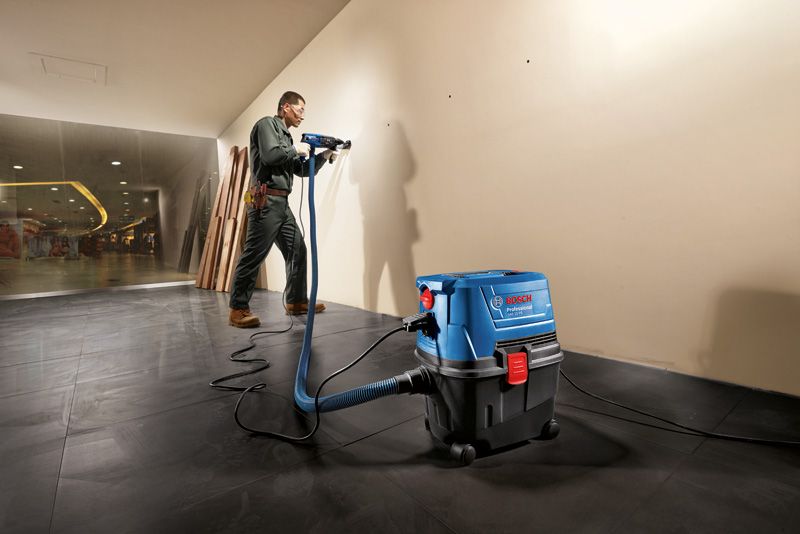 GAS 15 A person wearing safety equipment drills into a wall using a wet dry extractor.