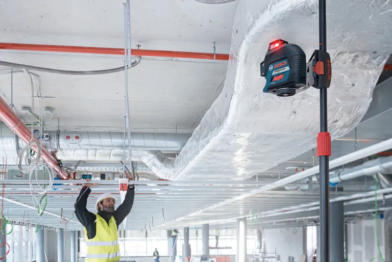 GLL 3-80 A person wearing safety equipment aligns ceiling frames using a laser leveling tool.