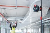 A person wearing safety equipment aligns ceiling frames using a laser leveling tool.