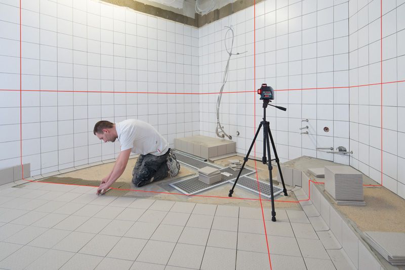 GLL 3-80 Person installing tiles in a bathroom using a laser leveling tool on a tripod.