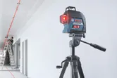 Laser leveling tool projects red lines across a ceiling as a person on a ladder works.