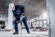 A person wearing safety equipment drills into concrete at a construction site.