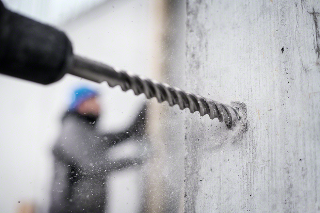 Person wearing safety equipment drills into a concrete wall.