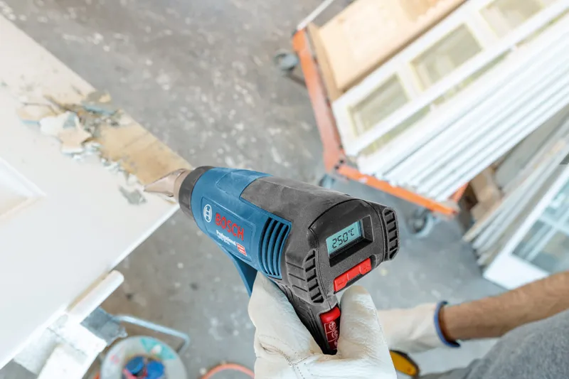 GHG 20-63 A person wearing safety equipment uses a heat gun to strip paint from a door.