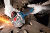 A person wearing safety equipment grinds a metal surface with an angle grinder, creating sparks.