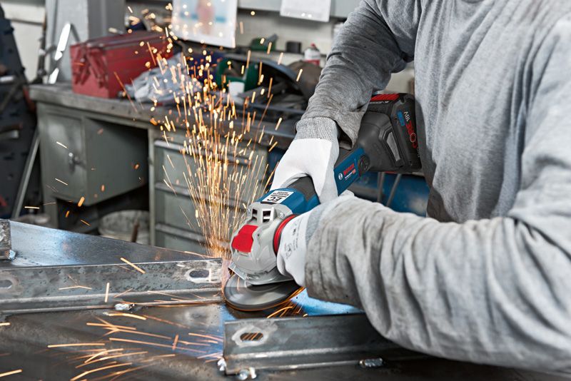 GWX 18V-10 C A person wearing safety equipment uses an angle grinder to cut metal, creating sparks.