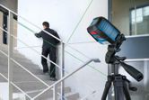 A person aligns stair railings using a green laser leveling tool on a tripod.