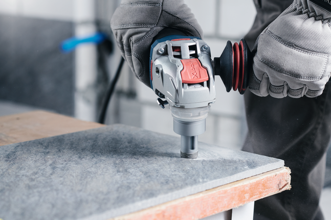 A person wearing safety equipment drills into a tile using a power tool.