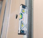Spirit level measuring vertical alignment on a metal stud and drywall panel.