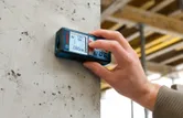 A person uses a laser measure to check distance on a concrete wall.