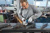 A person wearing safety equipment uses an angle grinder to cut a metal beam.