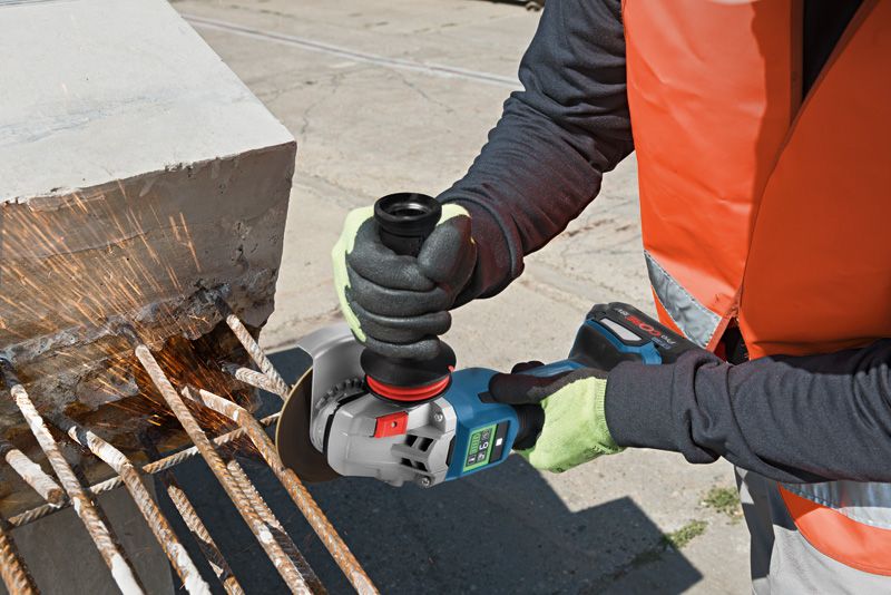A person wearing safety equipment grinds rebar extending from a concrete block.