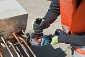 A person wearing safety equipment grinds rebar extending from a concrete block.