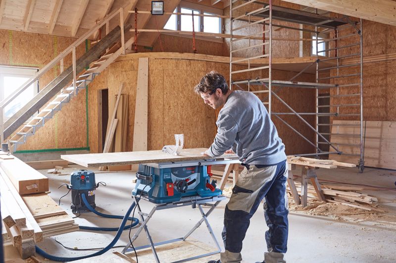 GTA 560 A person operates a table saw to cut wood in a partially constructed building.