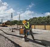 A person wearing safety equipment uses a reciprocating saw to cut a pipe at a construction site.