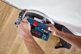A person operates a cordless circular saw to cut wood flooring near a wall.